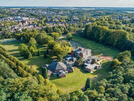 Vista aérea de una zona residencial con casas, un edificio grande con techo rojo y un campo verde.