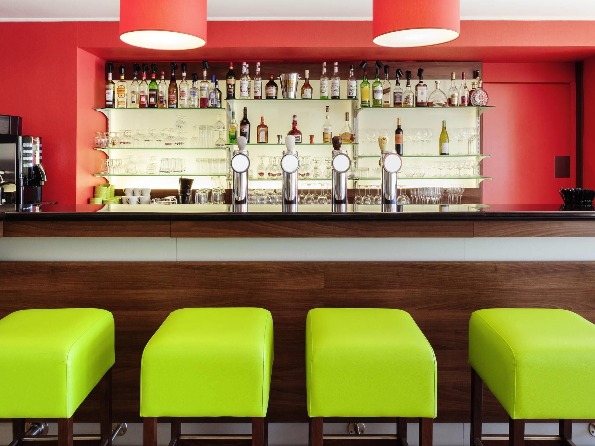A bar area with multiple liquor bottles and glasses, a coffee machine, and bright green bar stools.