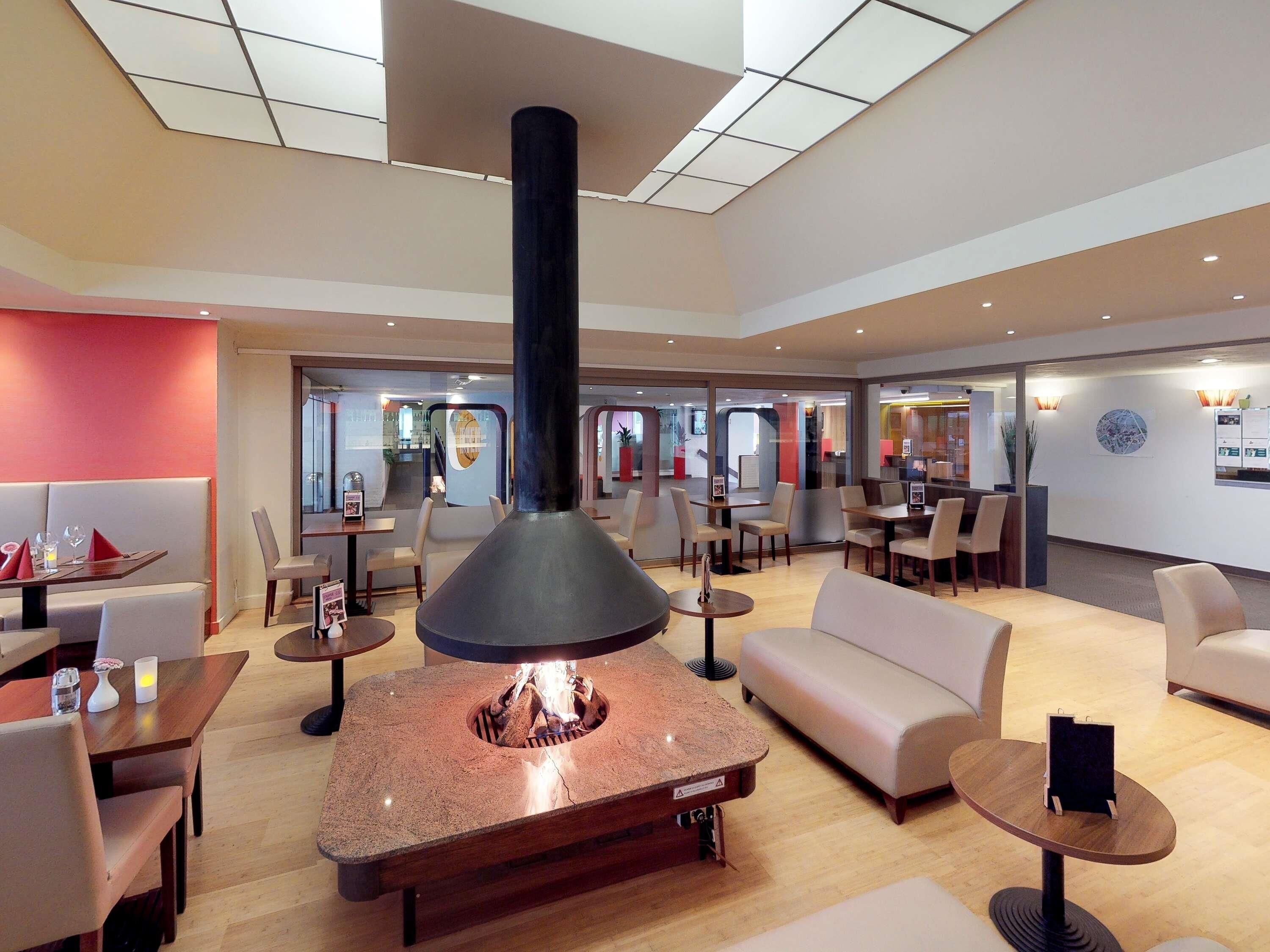 A modern hotel lobby with a central fireplace, seating areas, and a view of the interior.