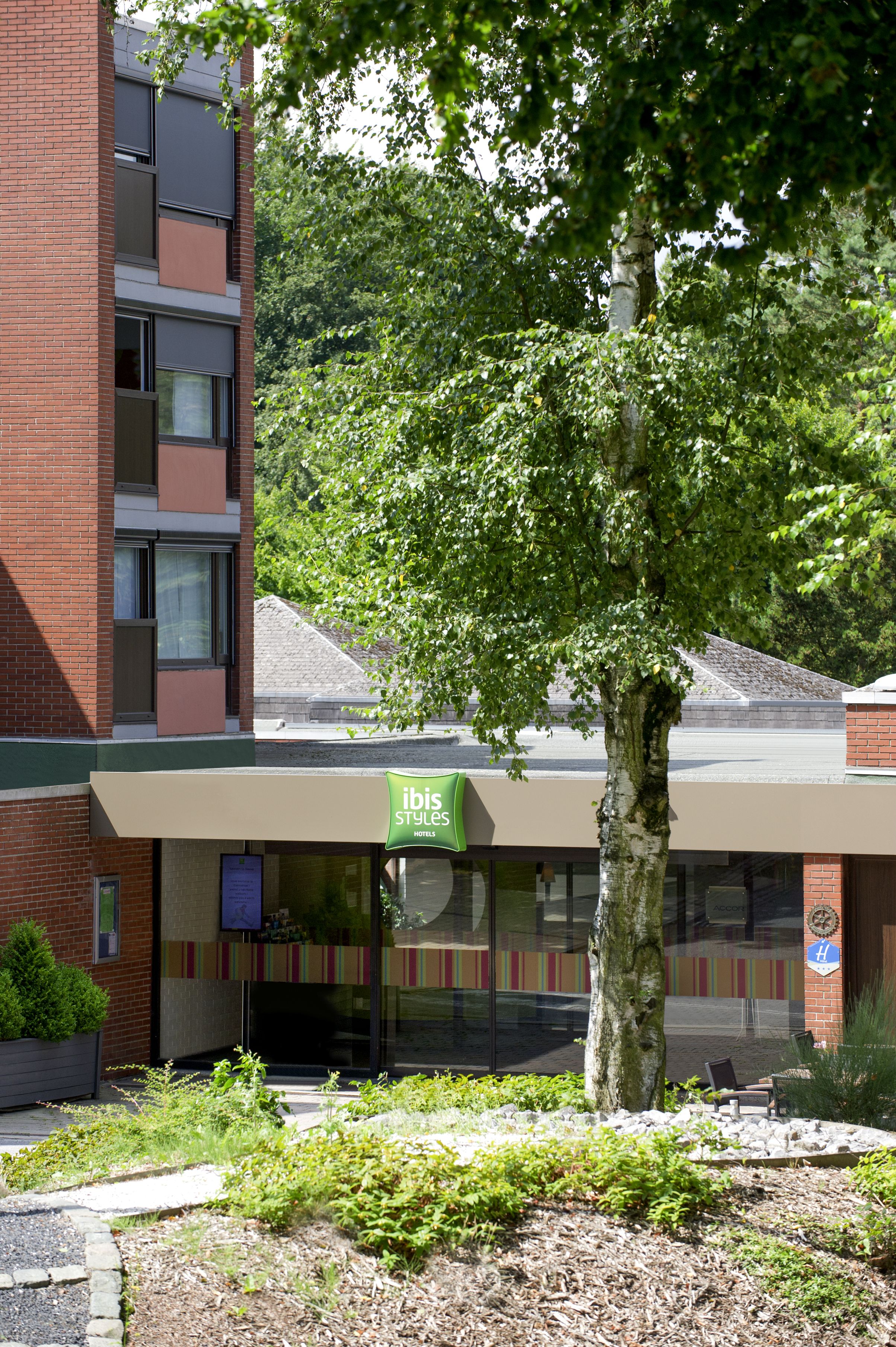 Un hotel con toldo verde, un árbol en primer plano y un edificio de ladrillo al fondo.