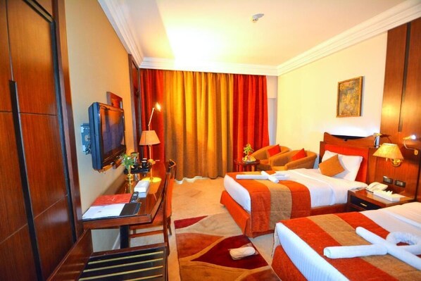 A hotel room with two beds, a desk, a TV, and a bathroom.