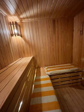 Een sauna met houten wanden en banken, een gestreept kleed en een wandlamp.