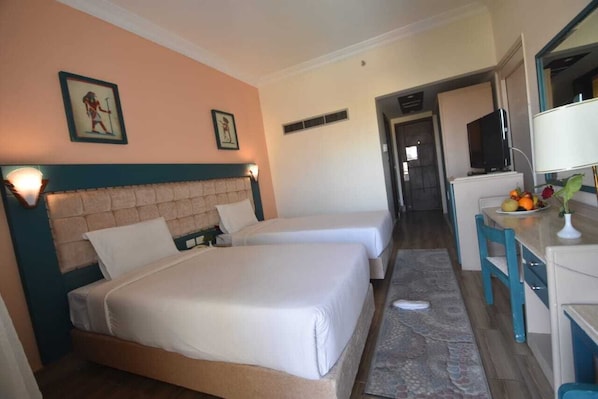 Habitación de hotel con dos camas, un escritorio con televisor y una pequeña kitchenette.