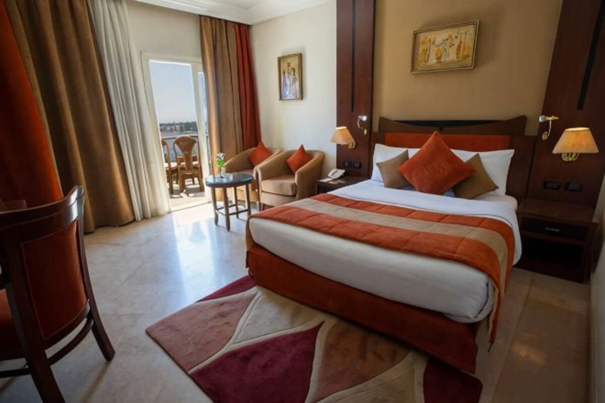 Een hotelkamer met een groot bed, een bureau, een stoel en uitzicht op een balkon.