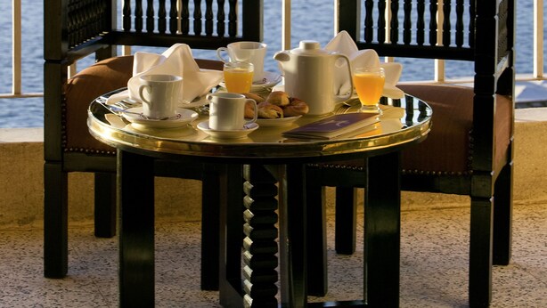 Une table dressée avec des aliments pour le petit-déjeuner, placée sur un balcon donnant sur un plan d’eau et sur des collines lointaines.