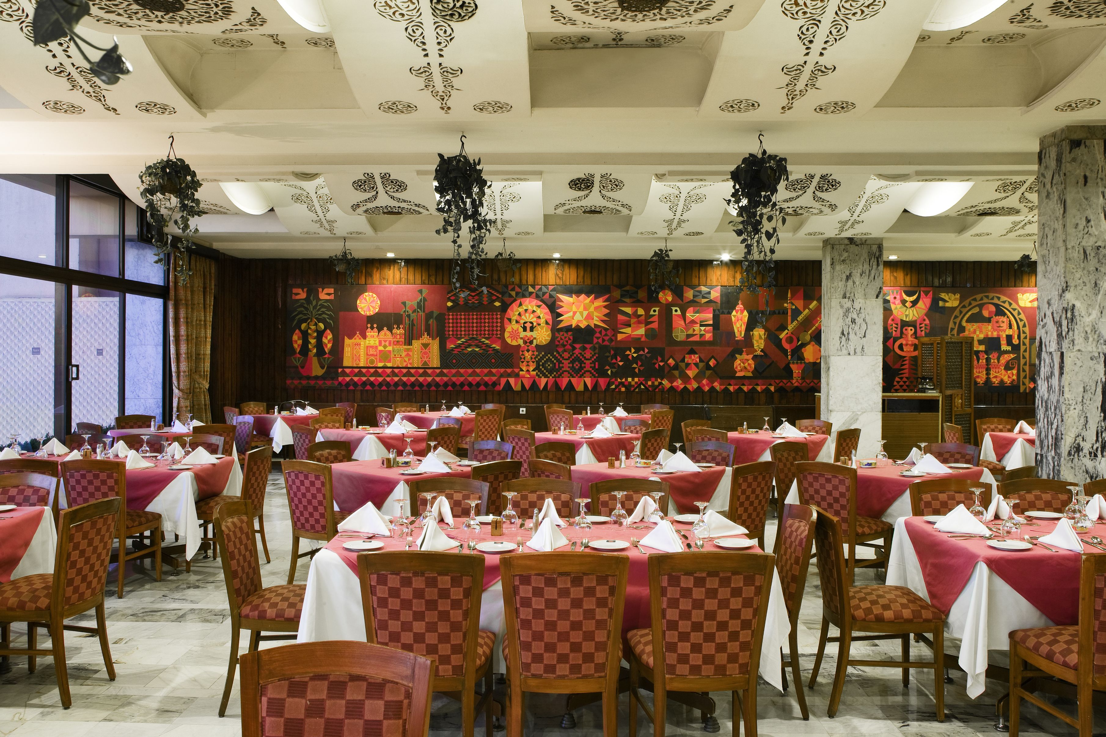 Un restaurante con mesas dispuestas para comer, con sillas estampadas y un techo decorativo.