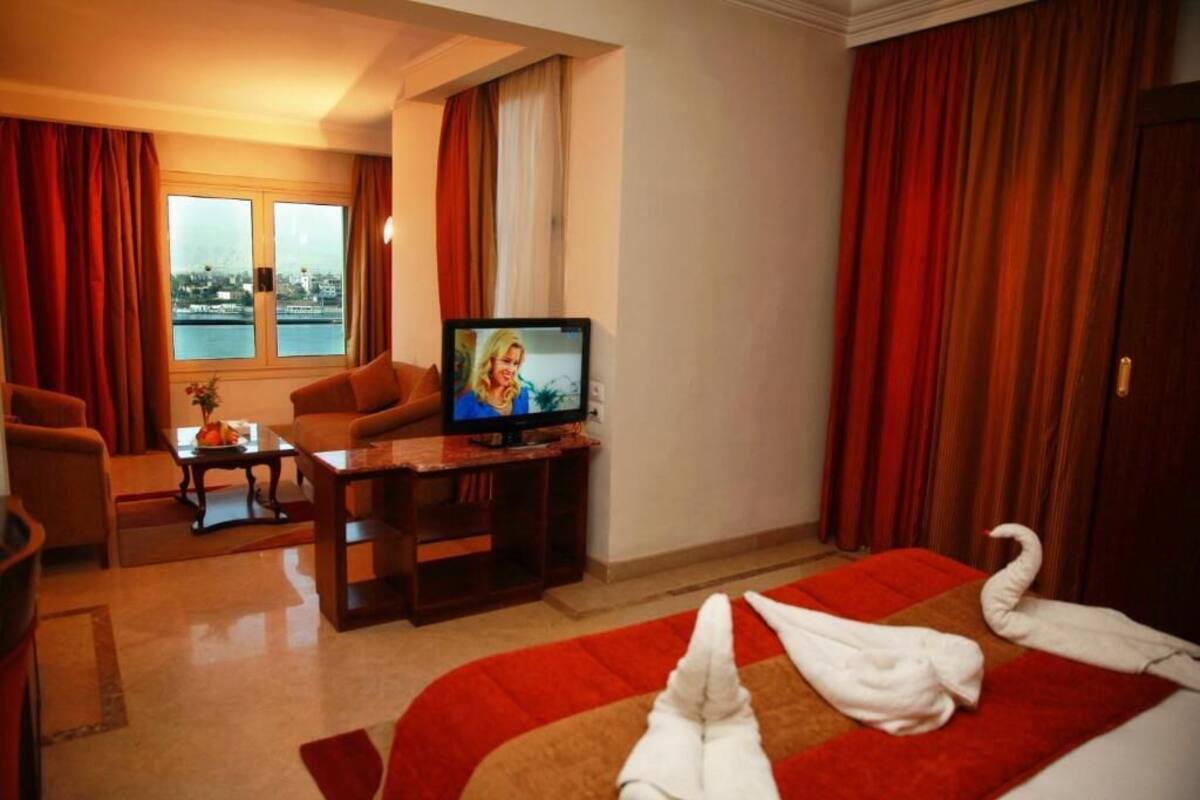A hotel room with a TV, a sofa, a desk, and a bed with towels.
