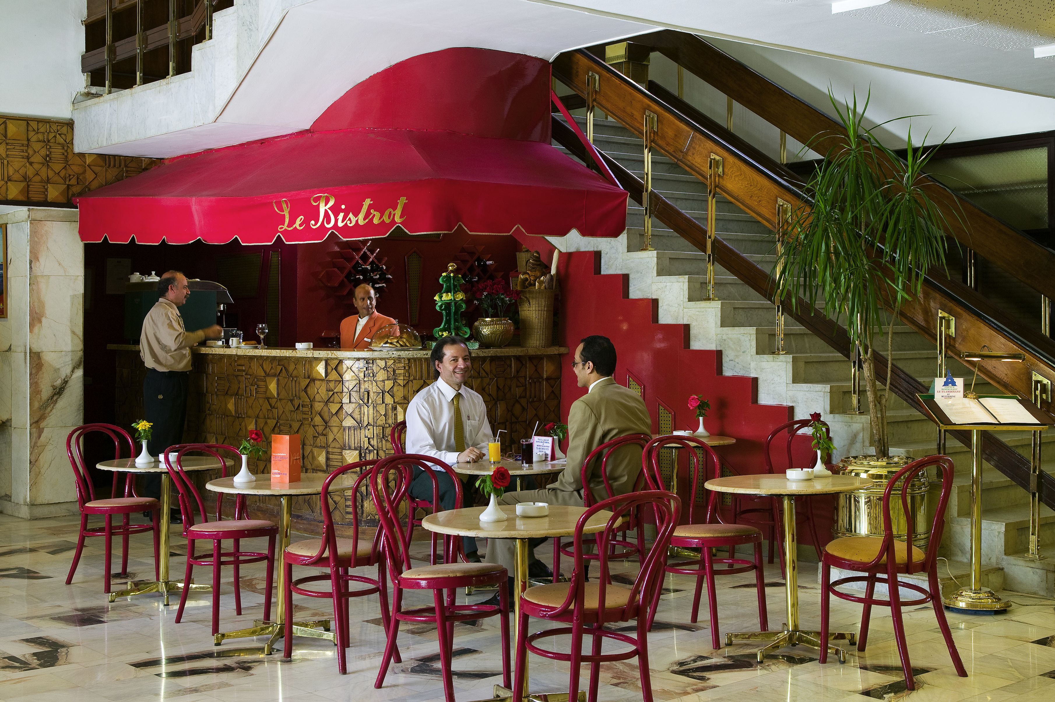 Ein Restaurant mit roten Stühlen und Tischen, einer Treppe und einer roten Markise mit dem Schriftzug 'Le Bistro'.