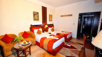 Habitación de hotel con dos camas, un sofá, una pequeña mesa con frutero y un televisor.