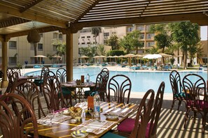 Un área de comedor junto a la piscina con mesas y sillas, con vistas a una piscina.