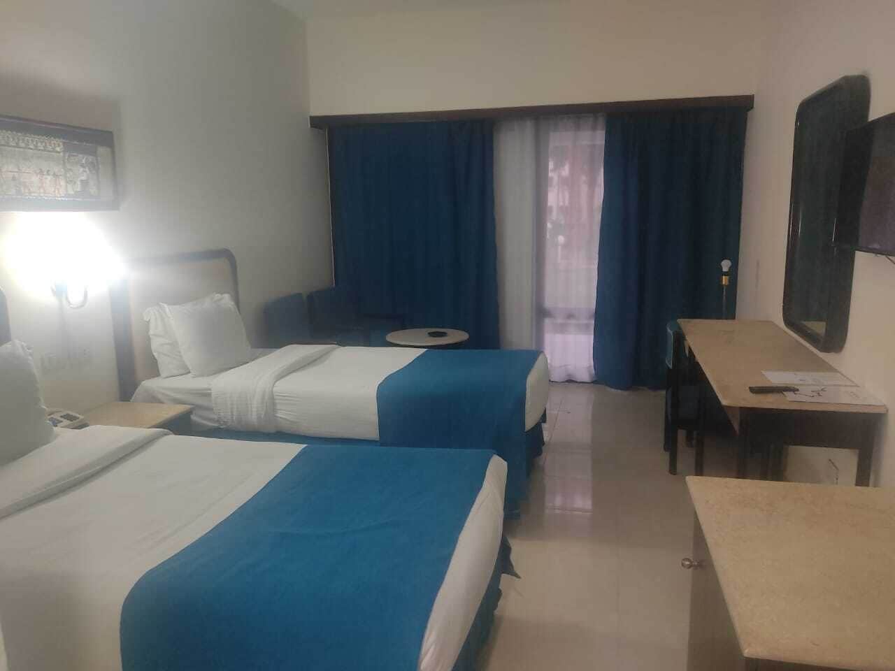 Habitación de hotel con dos camas, un escritorio, una silla y una ventana con cortinas.