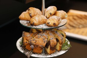 Una bandeja escalonada con pastelería, incluyendo croissants y muffins de chips de chocolate, espolvoreada con azúcar glas.