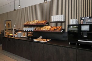 Un bufé de desayuno con diversas opciones de pastelería y pan, café y té, además de una pantalla digital con información del hotel.
