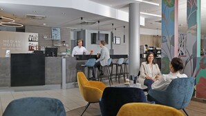 A modern hotel lobby with a reception desk, bar area, and seating for guests.