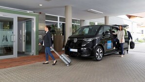 A black car with a luggage trolley parked outside a building with a glass door entrance.