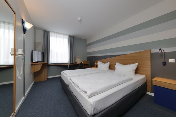 Una habitación de hotel con una cama grande, un escritorio con silla, un televisor y una ventana con cortinas.
