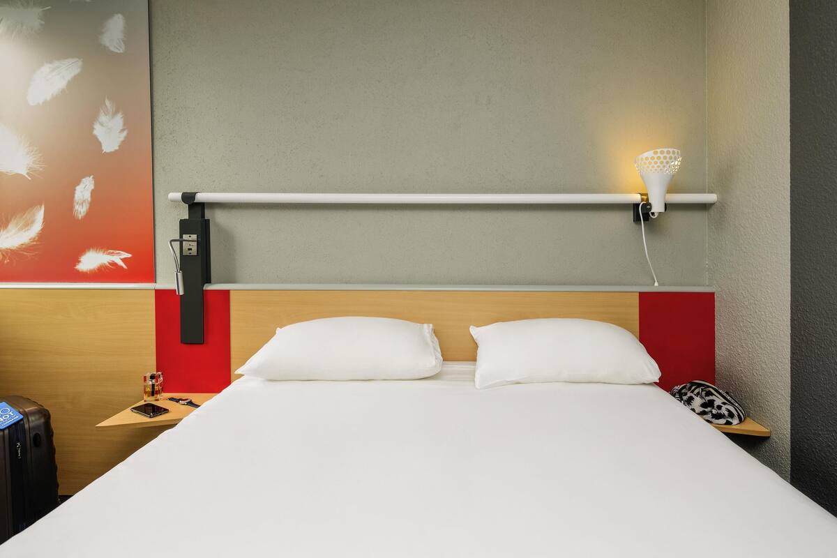 Ein Hotelzimmer mit einem Bett, einem Nachttisch, einer Lampe und einem Wandbild.