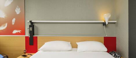 Una habitación de hotel con cama, mesita de noche, lámpara y una obra de arte en la pared.