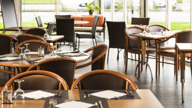 Restaurante com mesas postas para refeições, cadeiras e vista para o exterior.