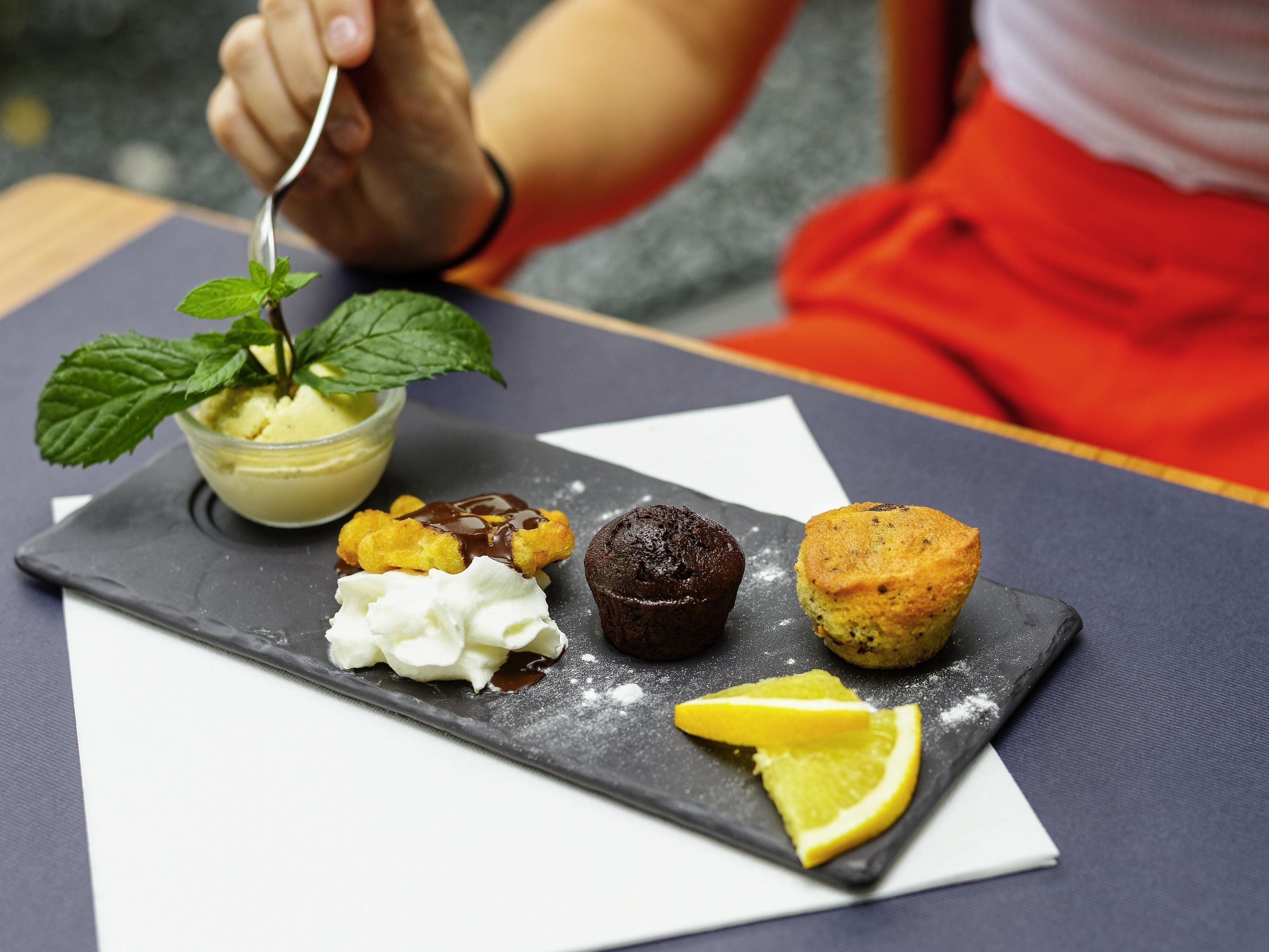 Um prato de sobremesa com sorvete, chantilly, um muffin de chocolate e fatias de limão.