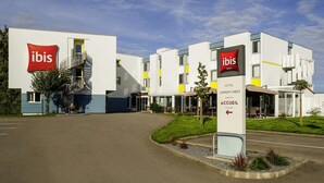 Um hotel moderno com um destaque para o letreiro 'ibis', uma escadaria e céu claro.
