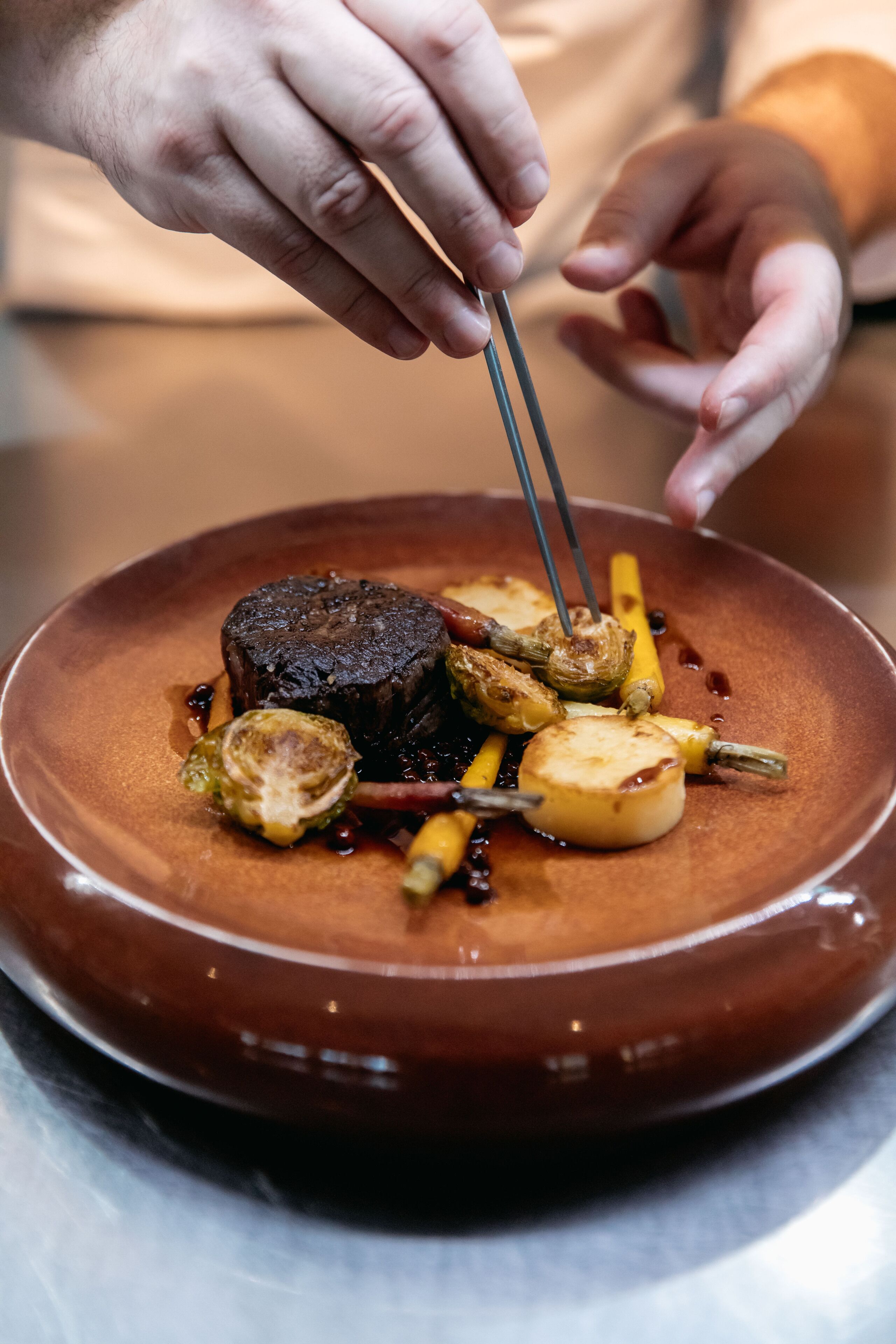 A person using tongs to serve a dish on a brown plate.