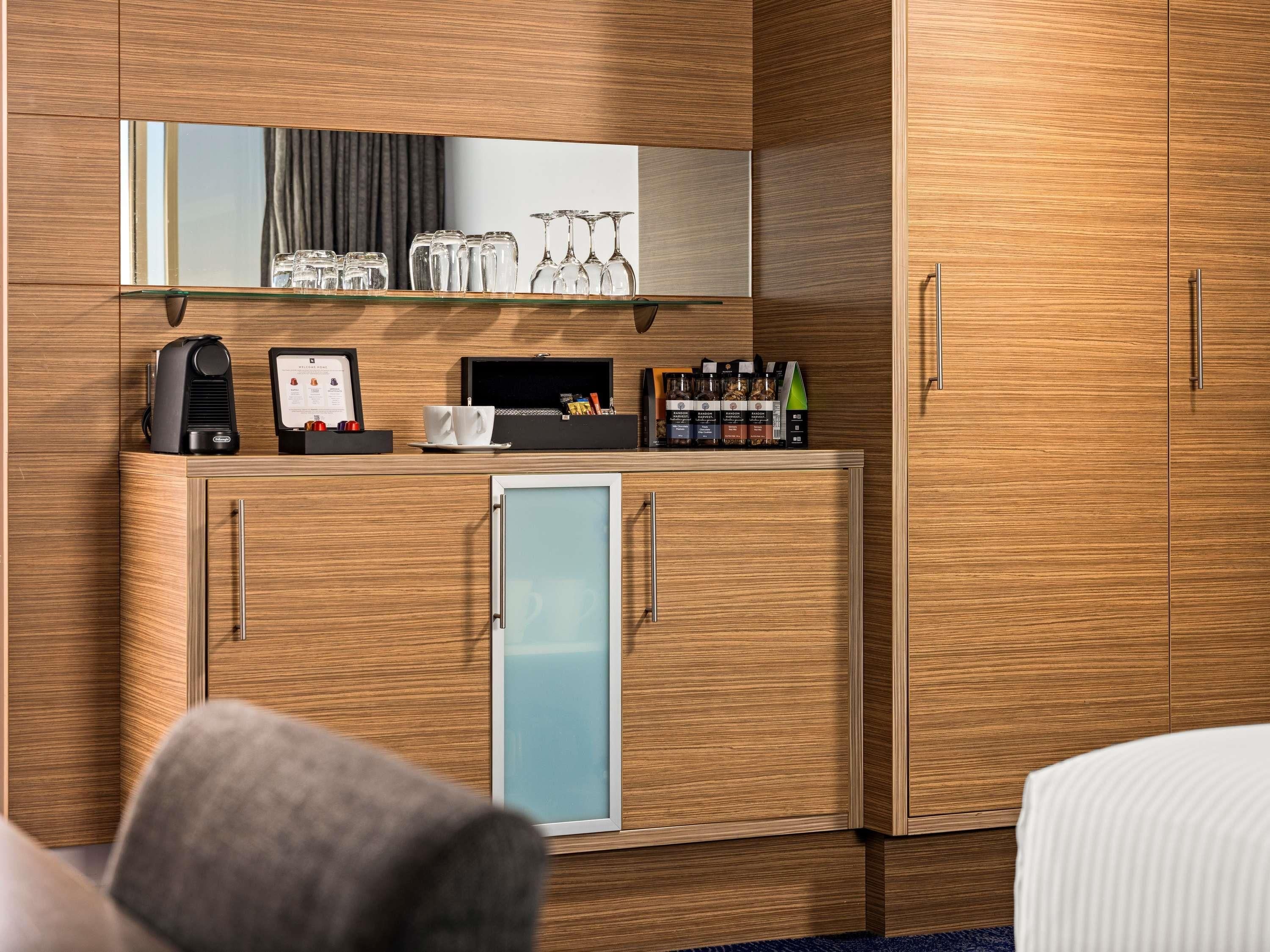 Een hotelkamer met een houten kastje, een minibar, een koffieapparaat en een kleine koelkast.