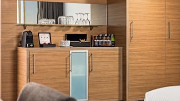 Een hotelkamer met een houten kastje, een minibar, een koffieapparaat en een kleine koelkast.