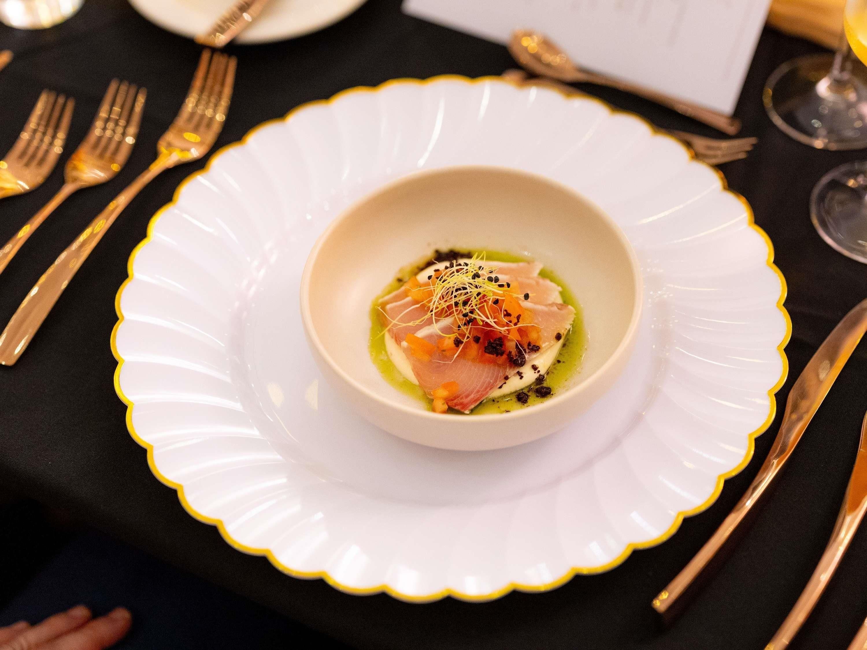 Un plato blanco con borde festoneado, un tazón de comida y una cuchara sobre una mesa.