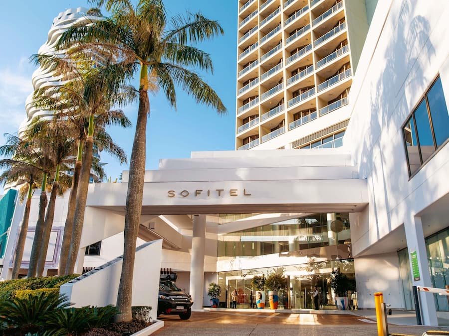Una entrada de hotel moderna con un letrero llamativo, palmeras y un área de estacionamiento.