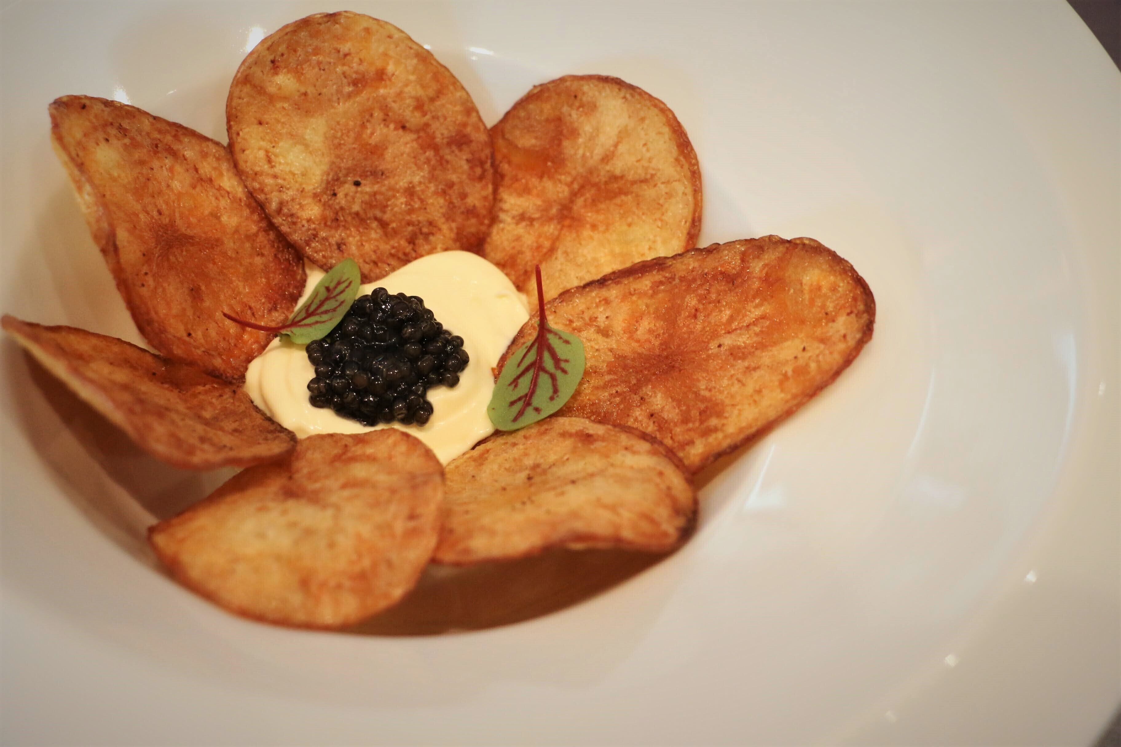 A plate with potato slices arranged in a flower shape, topped with a dollop of cream and black caviar.