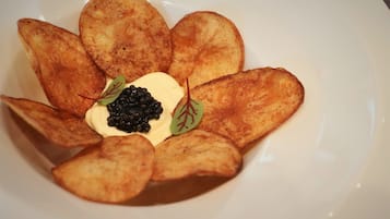 A plate with potato slices arranged in a flower shape, topped with a dollop of cream and black caviar.