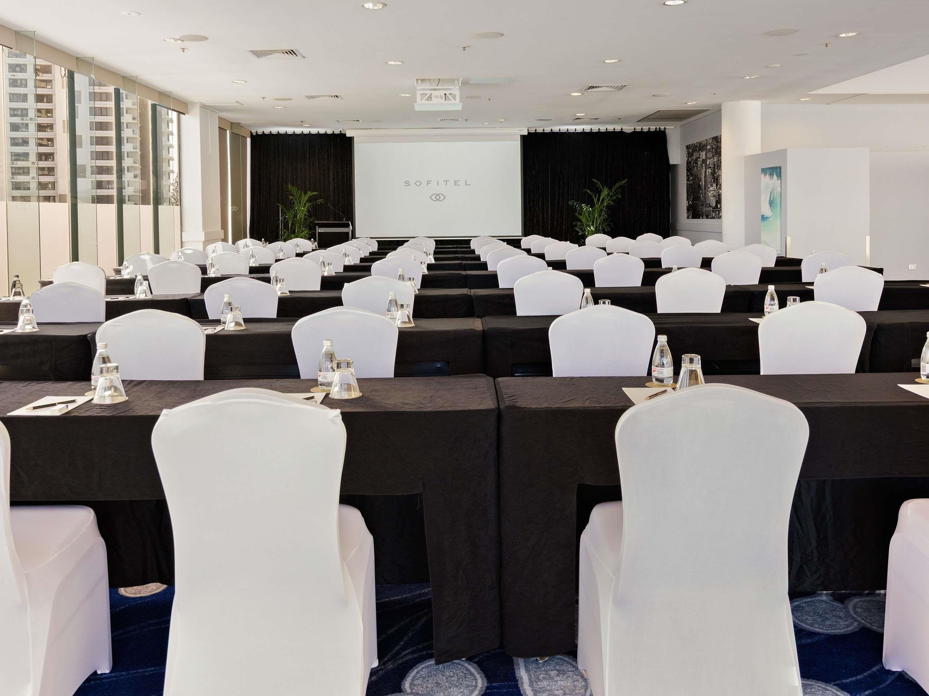 Ein Konferenzraum mit Reihen weißer Stühle, schwarzen Tischdecken und einer Bühne mit Bühnenbild.