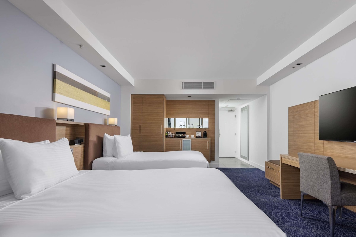 A hotel room with two beds, a desk, a television, and a minibar.