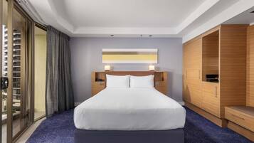 A hotel room with a large bed, a wooden wardrobe, a nightstand, and a view through a glass door.