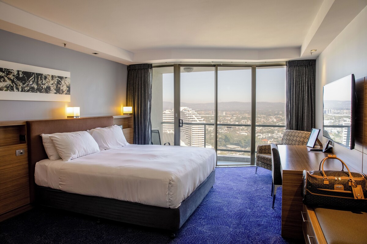 Une chambre d’hôtel avec un grand lit, un bureau, une chaise, une télévision et une vue sur la ville.