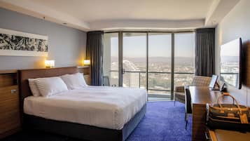 Habitación de hotel con una cama grande, un escritorio, una silla, un televisor y vistas de la ciudad.