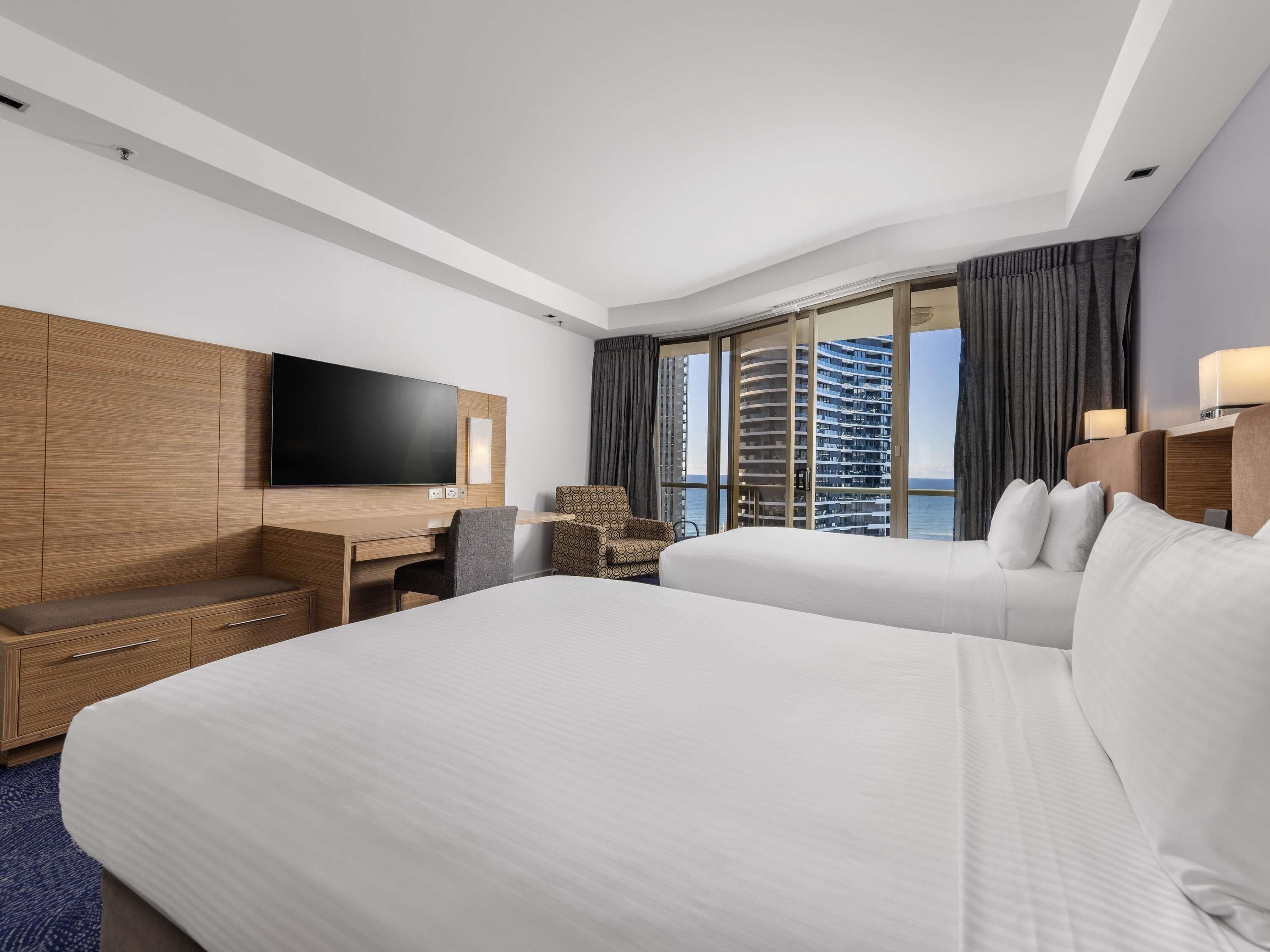 Una habitación de hotel con una cama grande, un escritorio con una silla, un televisor y vistas a un edificio de gran altura.