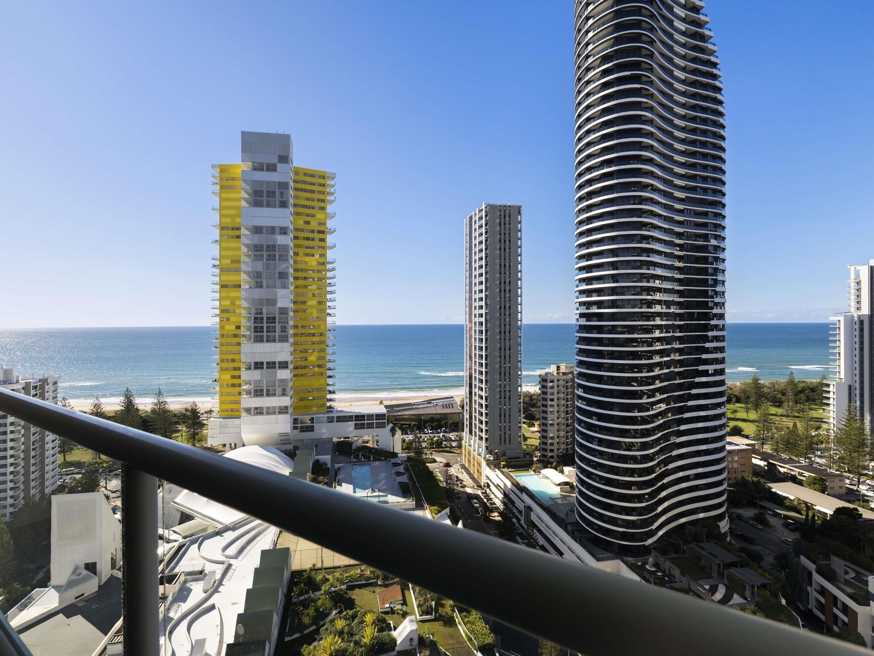 A coastal cityscape with modern high-rise buildings, a clear sky, and a beach in the background.