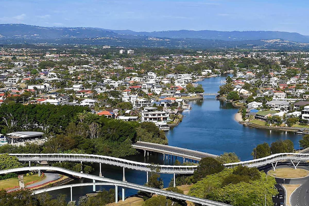 A river with bridges, a town with houses, and a mountain range in the background.