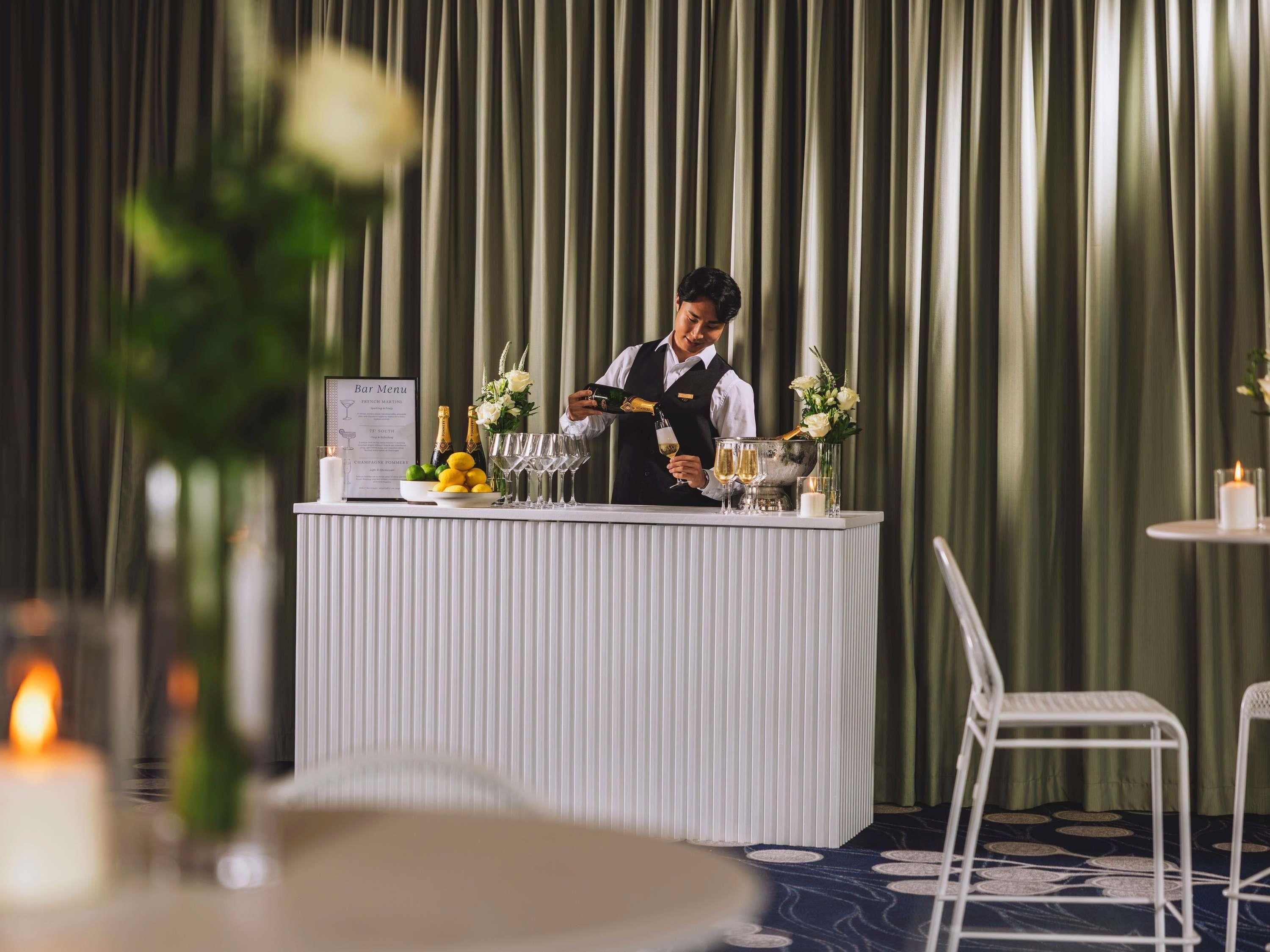 A bar area with a menu, bottles, glasses, and a waiter.