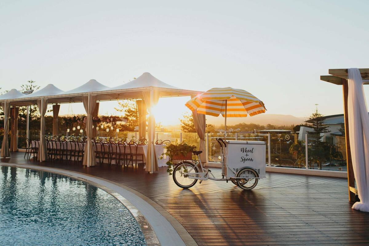 Un espace extérieur abrité, aménagé pour les repas, avec des tables et des chaises, une piscine et un chariot pour la livraison de vélos.