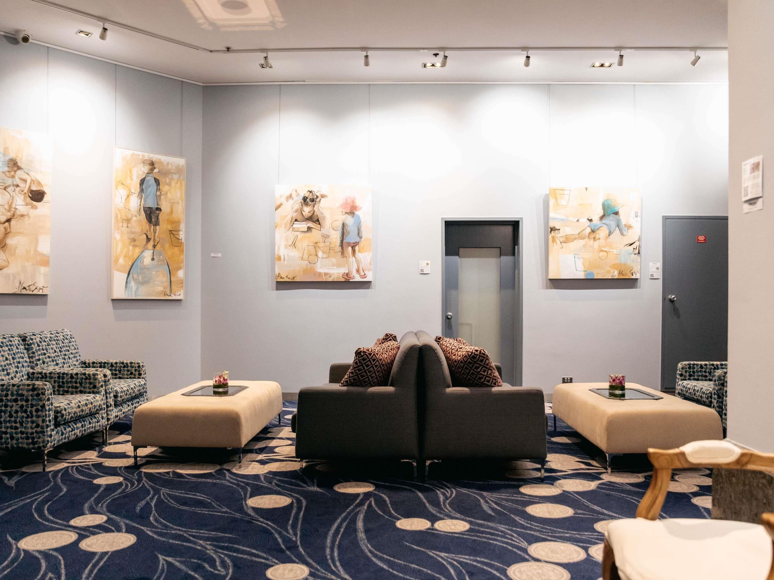 A hotel lobby with a blue patterned carpet, two sofas, a dark armchair, and artwork on the walls.
