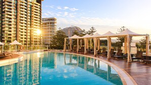 A swimming pool with lounge chairs and umbrellas, surrounded by high-rise buildings. - Sofitel Gold Coast Broadbeach (Broadbeach)
