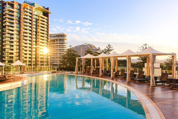 A swimming pool with lounge chairs and umbrellas, surrounded by high-rise buildings. - Sofitel Gold Coast Broadbeach (Broadbeach)