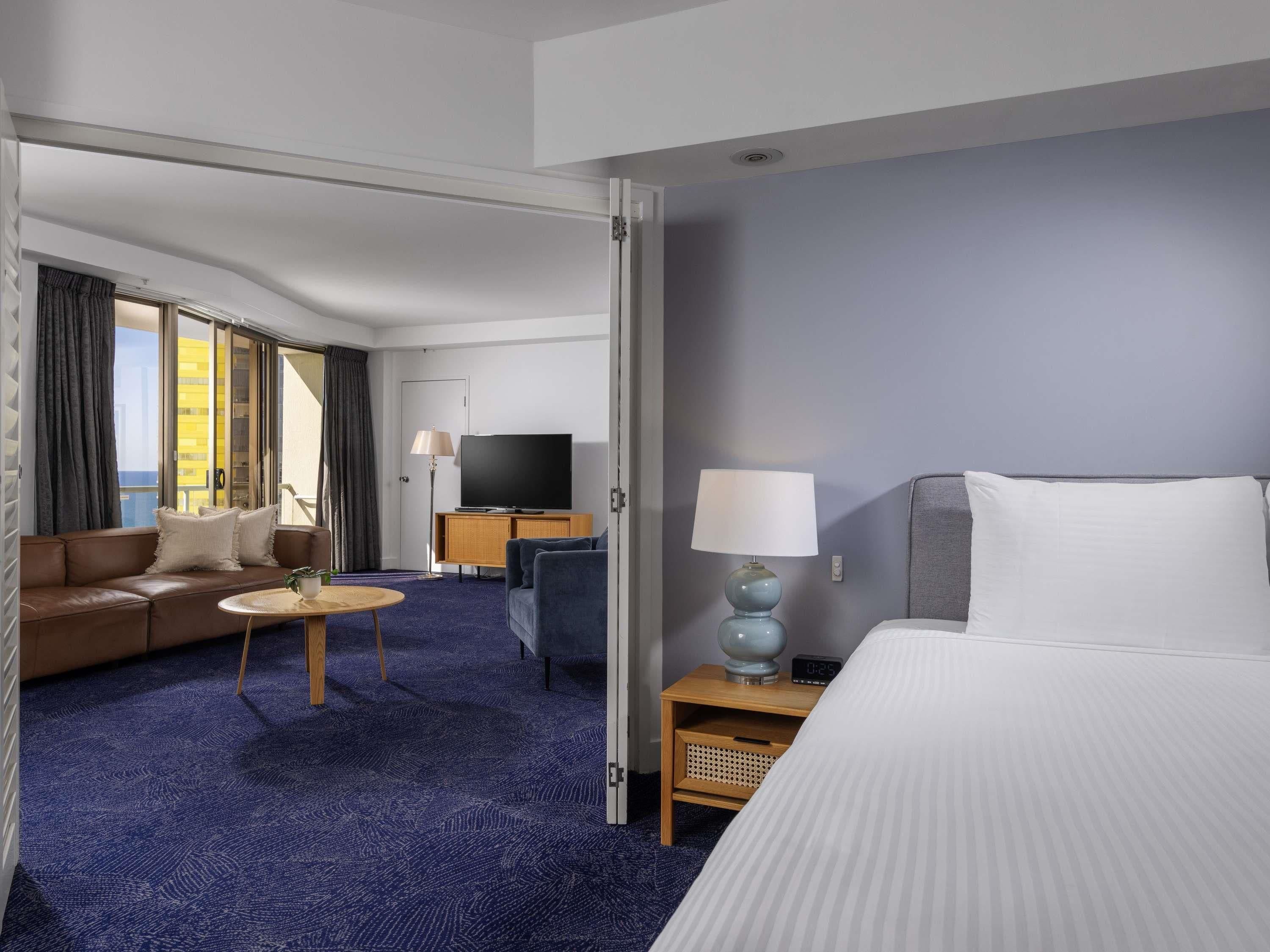 Habitación de hotel con cama, sofá, televisión, lámpara y una mesita.