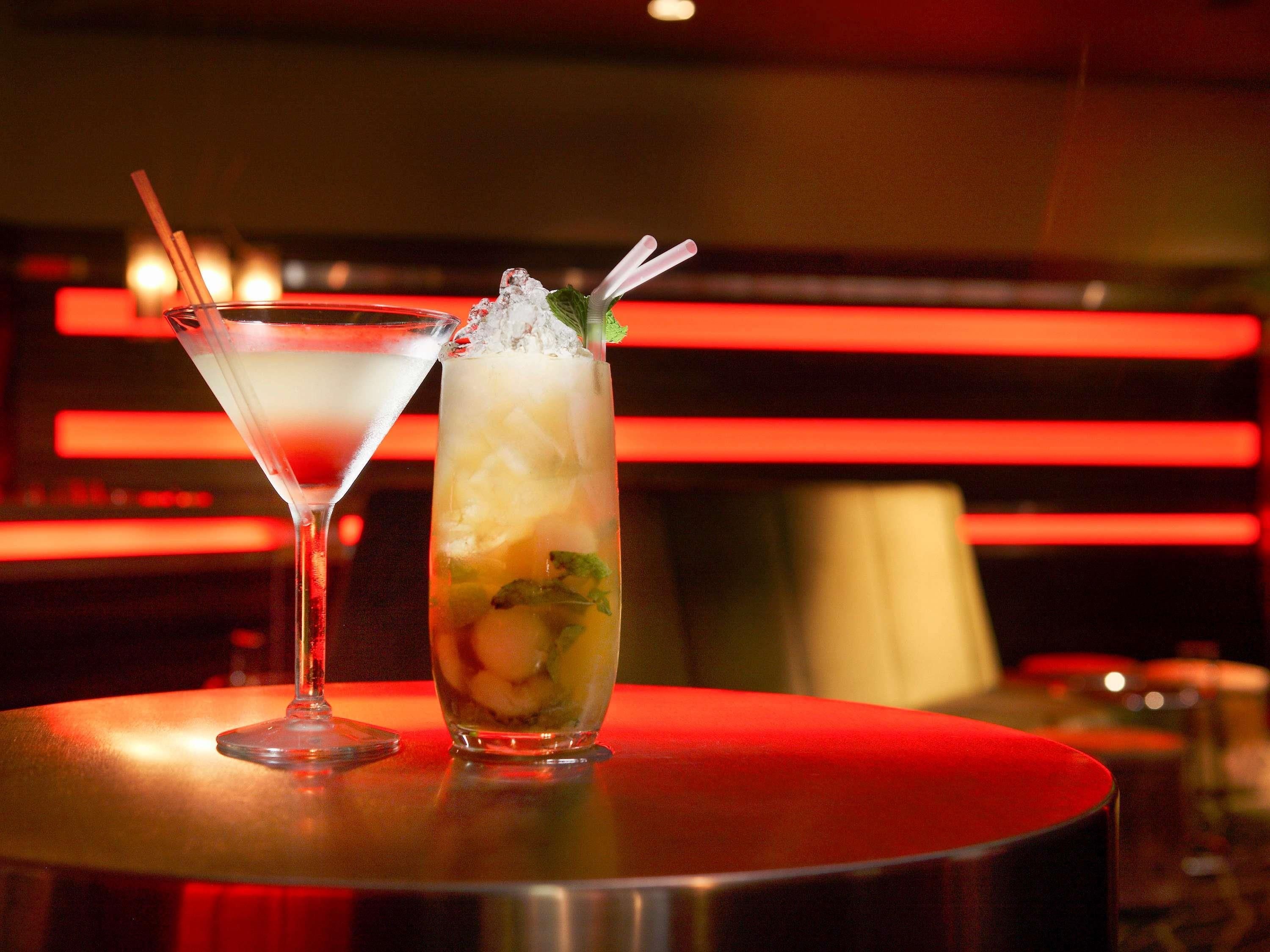 Two cocktails on a bar counter with a red-lit background.