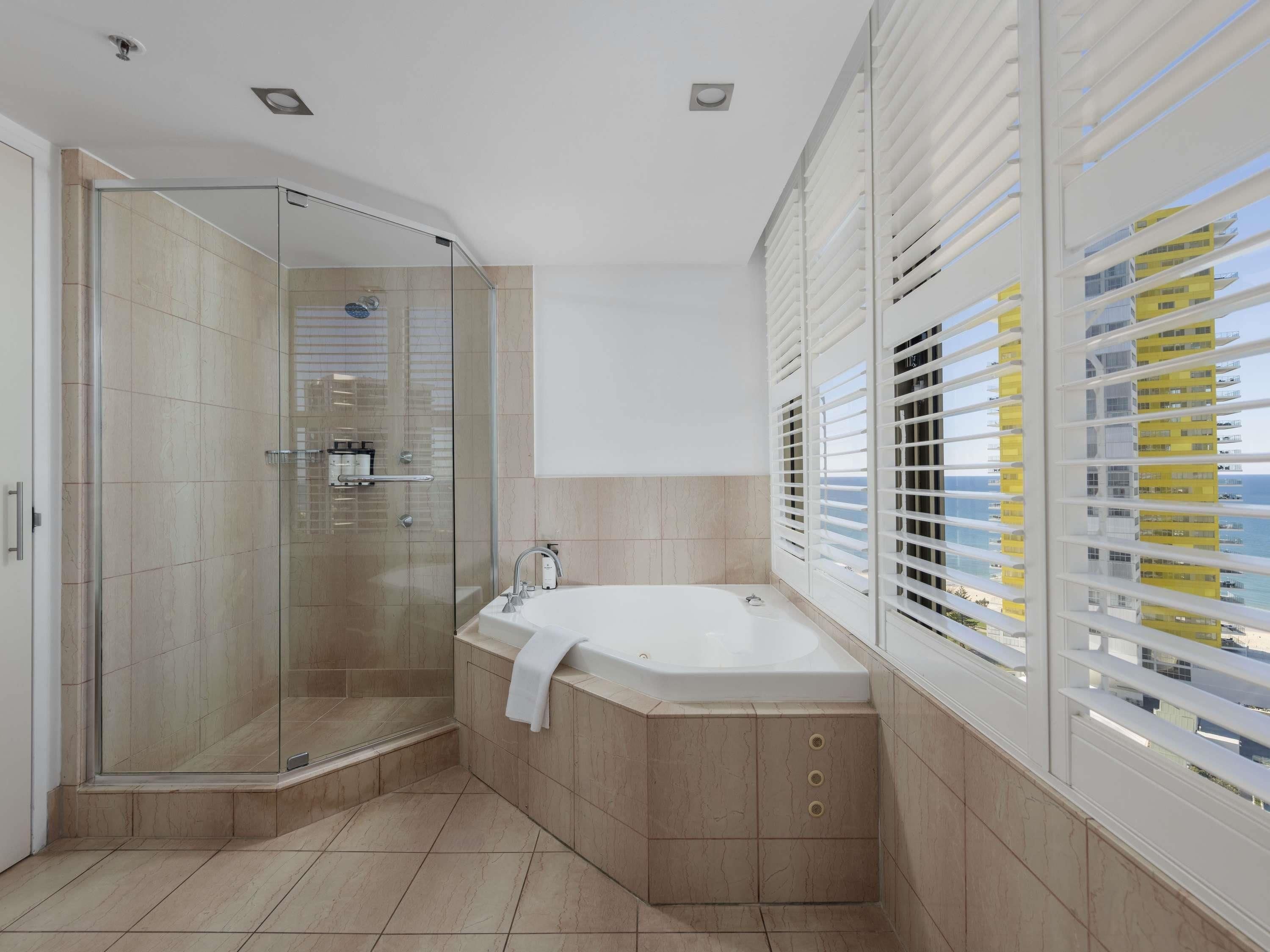 A modern bathroom with a glass-enclosed shower, a freestanding bathtub, and a view of a building through large windows.