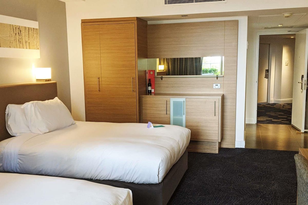A hotel room with a large bed, a wooden wardrobe, a minibar, and a mirror.