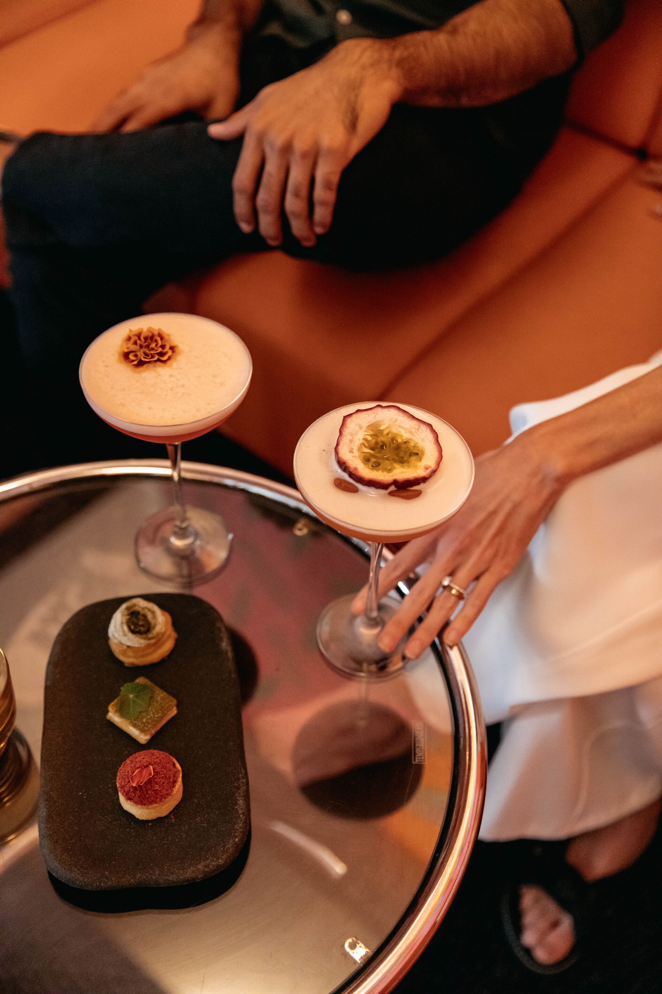 A table with three desserts and two cocktails on a glass table.